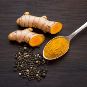 Cúrcuma fresca con pimienta negra en grano y cúrcuma en polvo en cuchara.