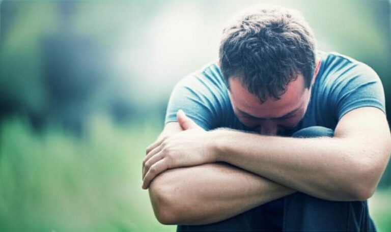 Hombre cabizbajo abrazando sus rodillas, representando el estrés y su impacto en el sistema inmunitario.