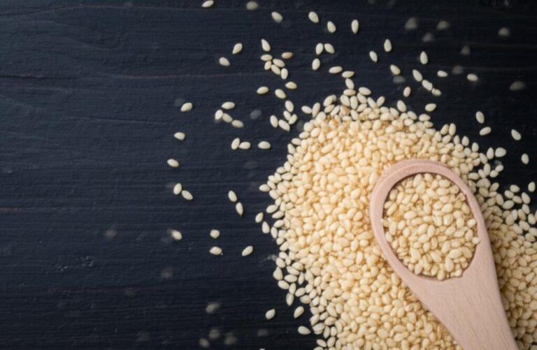 Semillas de ajonjolí dispuestas sobre una superficie oscura con una cuchara de madera, destacando su uso en la nutrición.