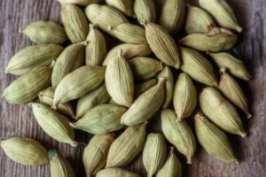 Primer plano de vainas de cardamomo verde sobre una superficie de madera, mostrando su textura y forma.