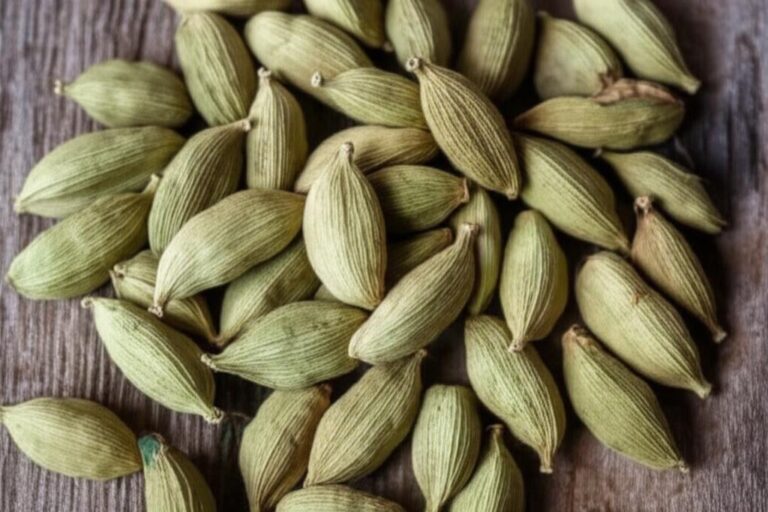 Primer plano de vainas de cardamomo verde sobre una superficie de madera, mostrando su textura y forma.