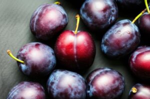 Imagen de ciruelas frescas y maduras sobre una superficie oscura.