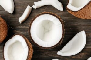 Coco fresco cortado sobre mesa de madera, mostrando la pulpa blanca y la cáscara marrón, ideal para información nutricional.