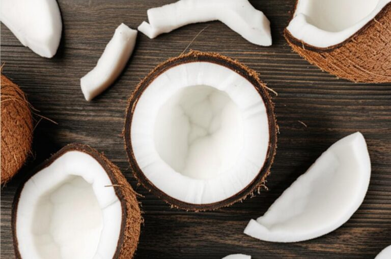 Coco fresco cortado sobre mesa de madera, mostrando la pulpa blanca y la cáscara marrón, ideal para información nutricional.