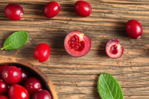 Arándanos rojos frescos sobre una mesa de madera, algunos enteros, otros cortados por la mitad mostrando su interior, con hojas verdes.