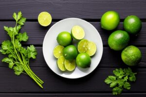 Imagen de limas frescas enteras y en rodajas en un plato blanco junto con cilantro sobre una mesa de madera oscura, representando los beneficios nutricionales de la lima.