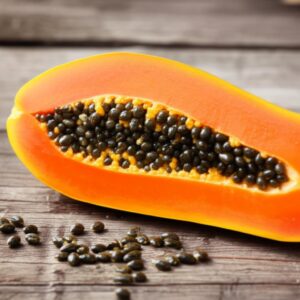 Papaya cortada por la mitad mostrando sus semillas negras sobre una mesa de madera.