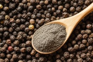 Cuchara de madera con pimienta negra molida sobre granos de pimienta negra enteros
