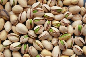 Fotografía de primer plano de pistachos con cáscara, mostrando el fruto verde en algunos ejemplares.