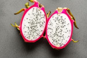 Dos mitades de pitahaya mostrando la pulpa blanca con semillas negras sobre fondo gris