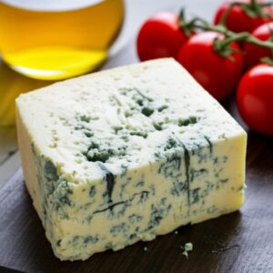 Primer plano de un bloque de queso azul con tomate cherry y aceite de oliva al fondo.