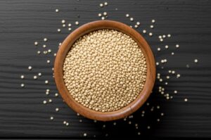Tazón de madera lleno de granos de quinua cruda sobre un fondo negro, para información nutricional.