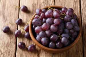 Uvas rojas frescas en un tazón de madera sobre mesa de madera.