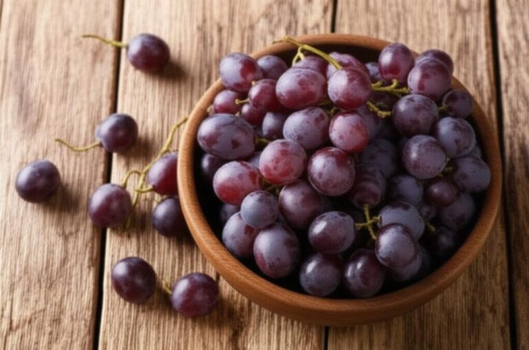 Uvas rojas frescas en un tazón de madera sobre mesa de madera.