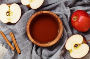 Vinagre de manzana sin filtrar en cuenco de madera con manzanas y canela