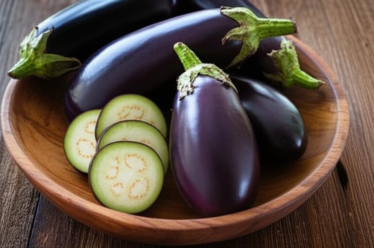 Imagen de berenjenas frescas enteras y en rodajas en un tazón de madera